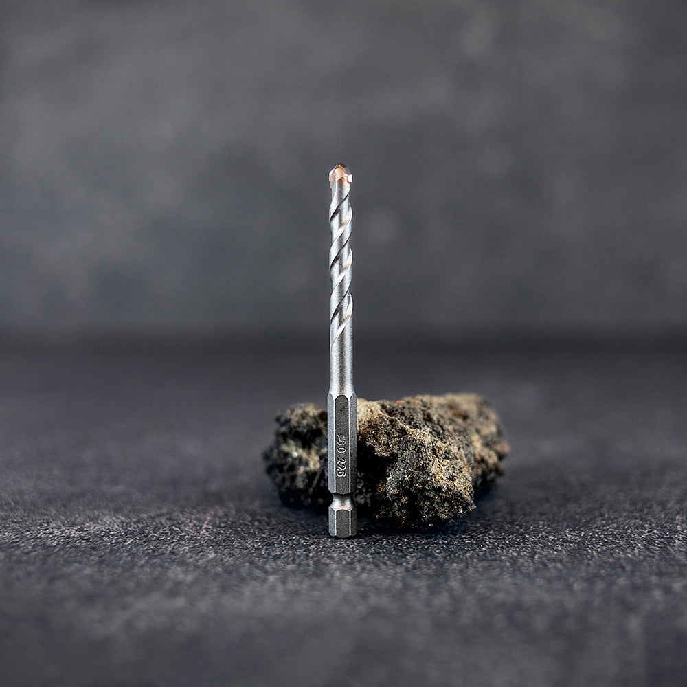 Ett klinkerborr 6 mm som står rakt upp framför en mindre sten, mörk klinkerbakgrund