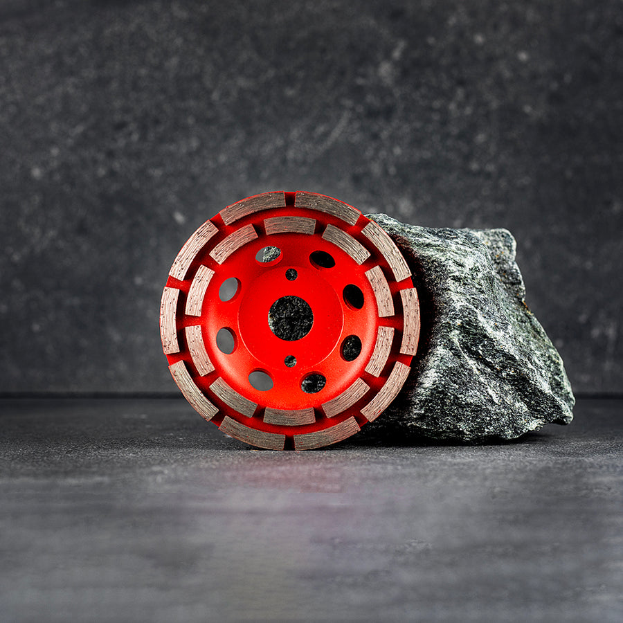 En röd slipskål som står upp lutad mot en sten, mörk klinkerbakgrund